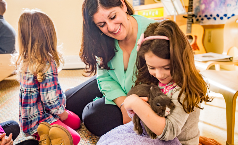 a_nursery_teacher_with_two_children_one_of_them_holding_a_bunny