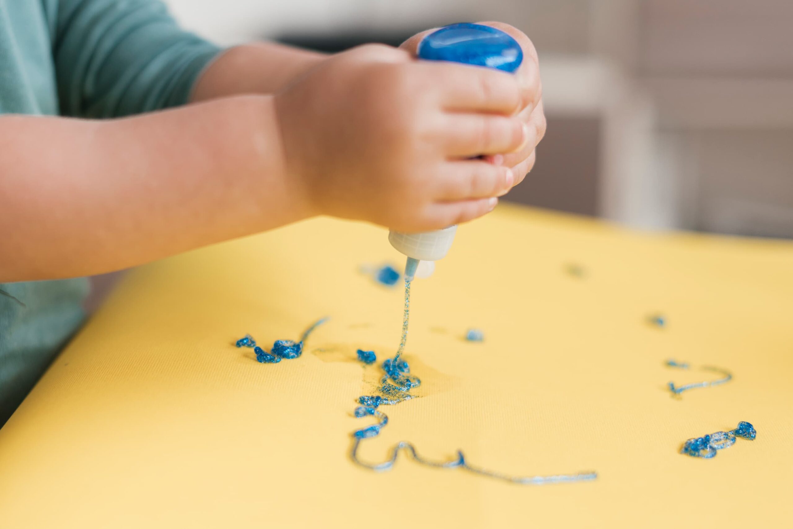 bambino che dipinge con colla glitterata per creare embossing su un foglio giallo