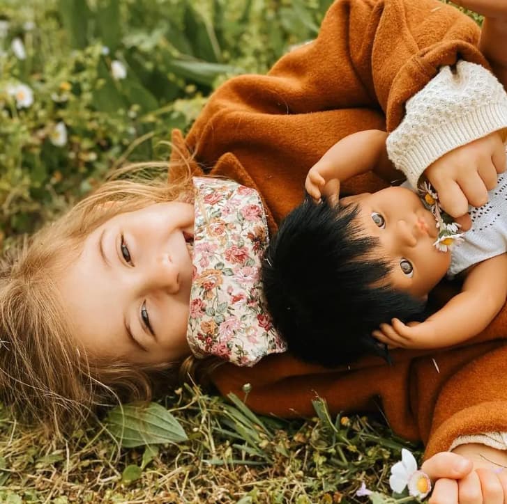 bambina che stringe a se una bambola. Sono distese nel prato verde