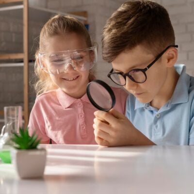 due bambini che giocano con giochi di scienze. Il bambino ha una lente di ingrandimento in mano e la bambina indossa degli occhiali per proteggersi