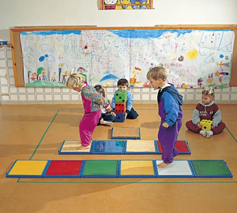 bambini che giocano con materiali tattili a terra quadrettati