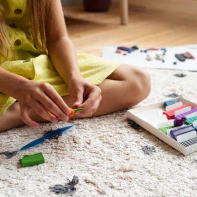 bambina che gioca con carta e colori sul pavimento