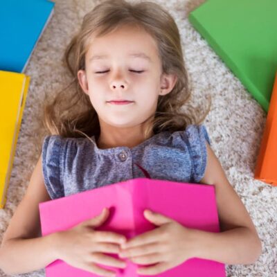 bambina distesa con occhi chiusi e libri attorno