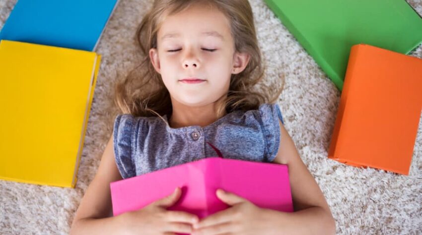 bambina distesa con occhi chiusi e libri attorno