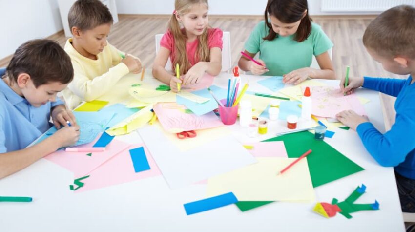 bambini che giocano/disegnano insieme radunati attorno ad un tavolo